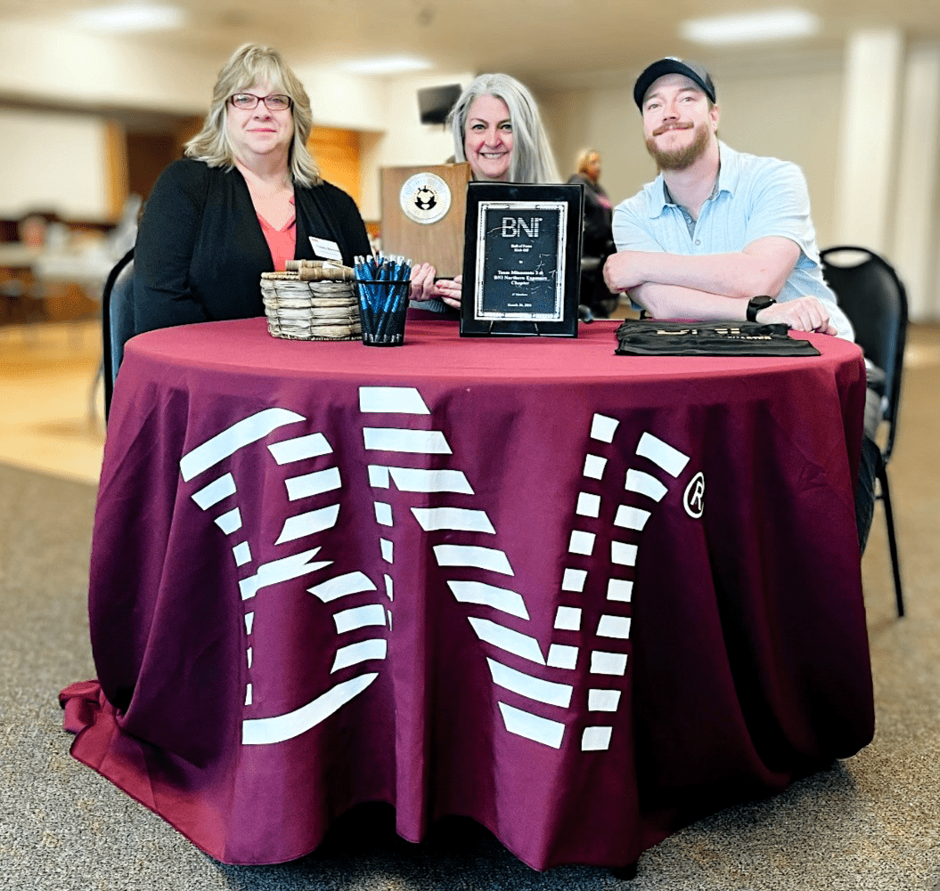 Pinnacle Marketing Group employee sitting at a BNI event table with awards and materials displayed.